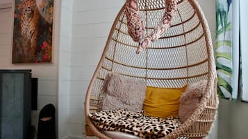 Een hangstoel met een gevlochten zitplaats en rugleuning, een kussen met luipaardprint en een pluizig kussen.