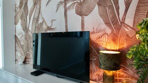 A television on a stand with a wall mural of tropical foliage behind it. - Costa Rica - Tropical immersion (Profondeville)