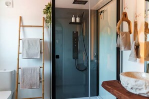 A modern bathroom with a glass shower enclosure, a bamboo towel rack, and a wooden vanity with a marble basin.