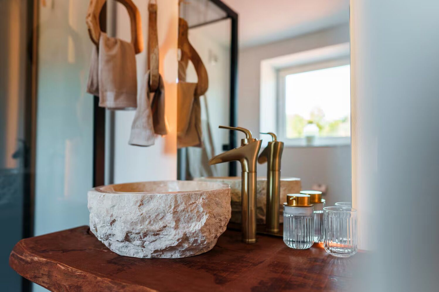 Une salle de bain rustique avec un grand lavabo en pierre, des robinets dorés et un plan de toilette en bois.