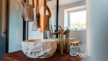 Une salle de bain rustique avec un grand lavabo en pierre, des robinets dorés et un plan de toilette en bois.