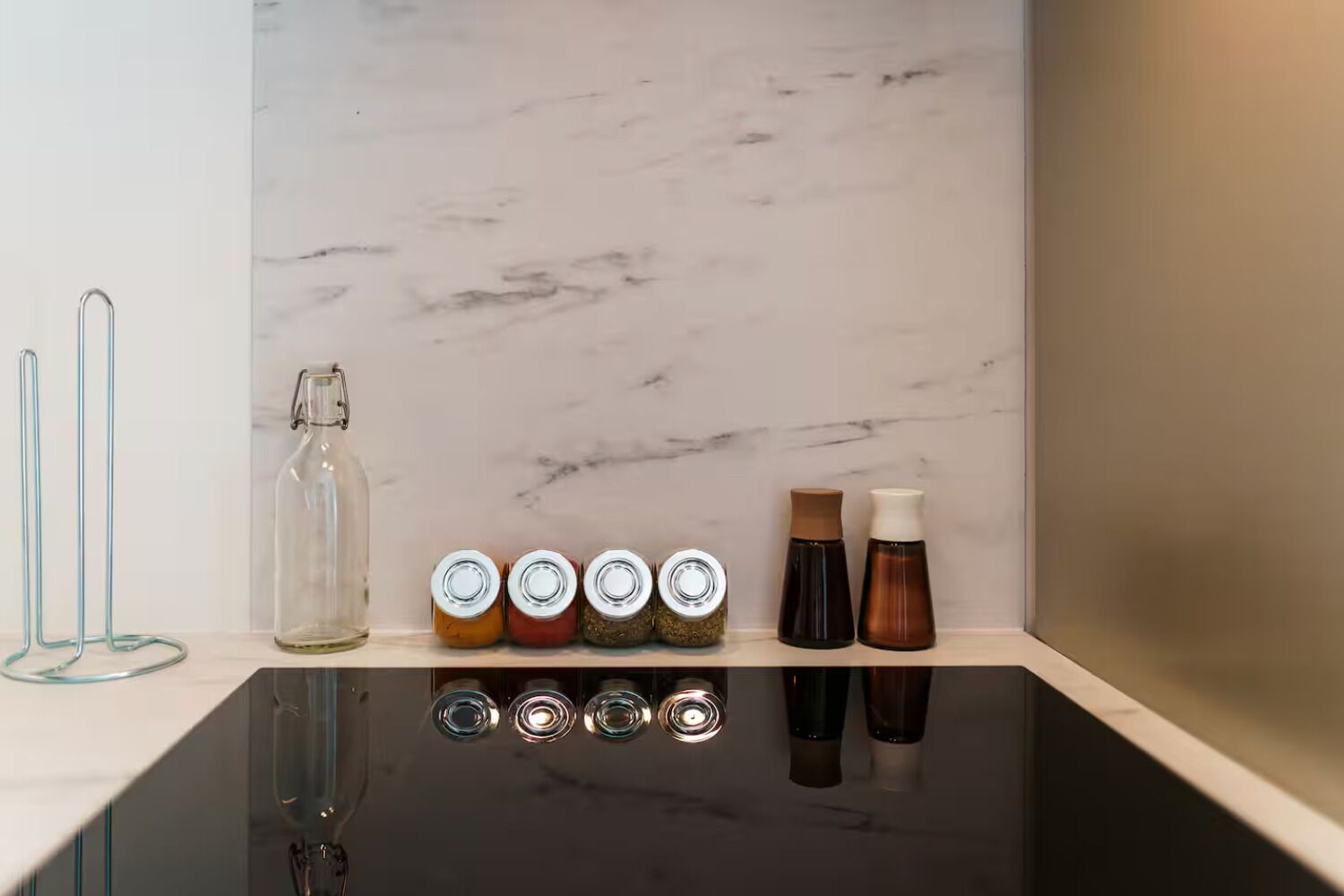 Un comptoir de cuisine avec un pare-feu en marbre, une bouteille en verre et quatre pots à épices.