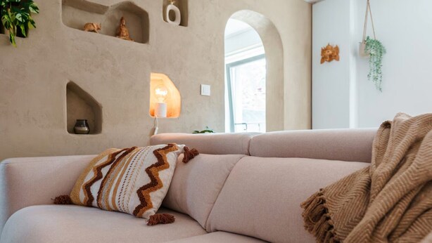 A beige sofa with a patterned pillow and a throw blanket, a wall-mounted shelf with a statue, and a hanging plant. - Le Bali - Zen & serenity (Profondeville)