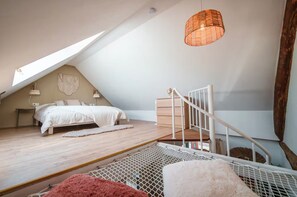 A bedroom with a sloped ceiling, a bed, a staircase, and a hanging light fixture.