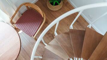 A spiral staircase with wooden steps and a white railing, a wicker chair with a red cushion, and a potted plant on the floor.