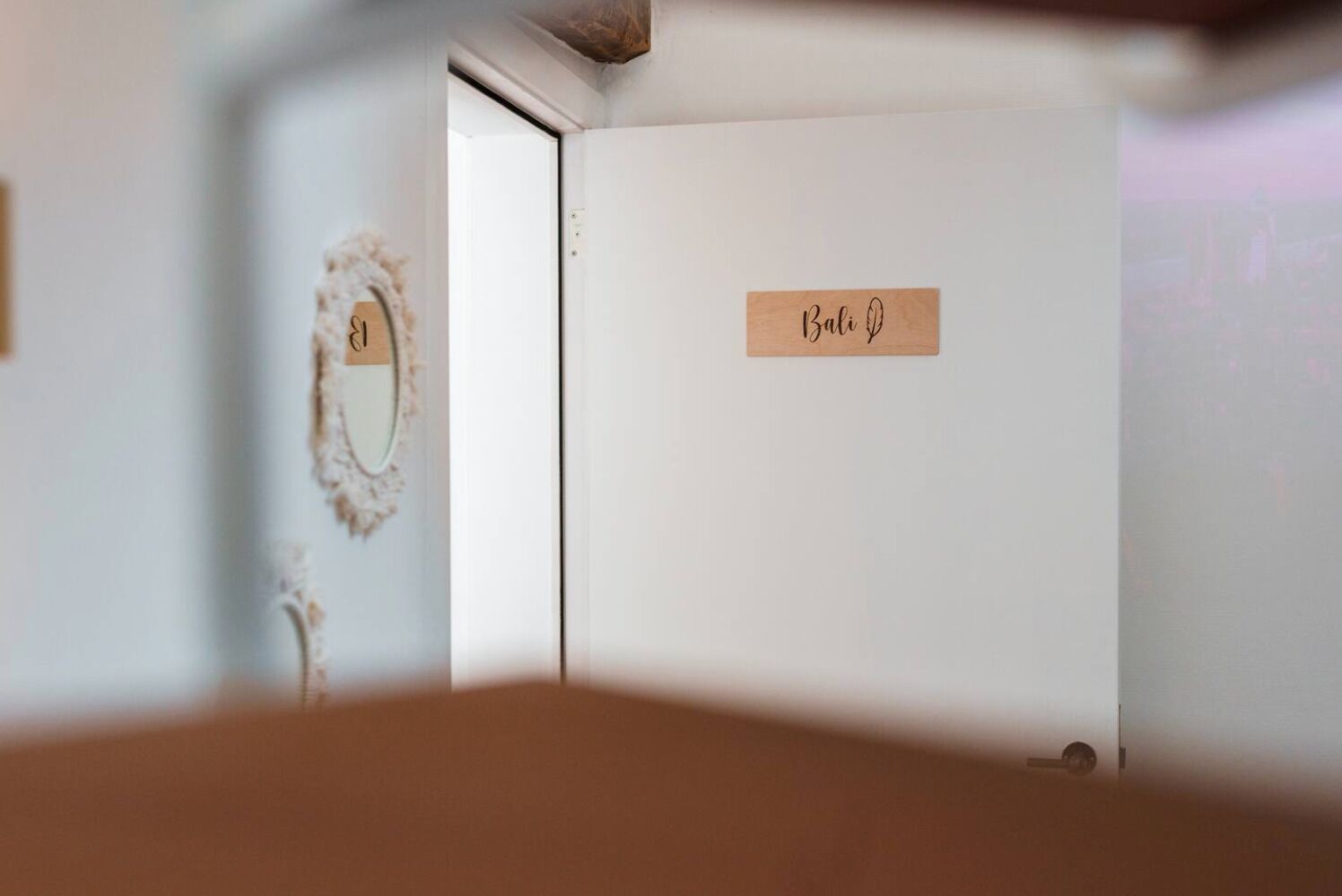 Une pièce avec une porte blanche, une plaque nominative en bois portant l’inscription « Bali », et un miroir fixé au mur.