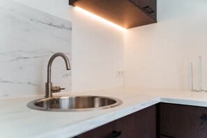 Een moderne keuken met een roestvrijstalen spoelbak, een marmeren achterwand en verlichting onder de kastjes.