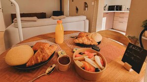 A breakfast table with croissants, a fruit bowl, a juice bottle, and a sign welcoming guests. - Le Bali - Zen & serenity (Profondeville)