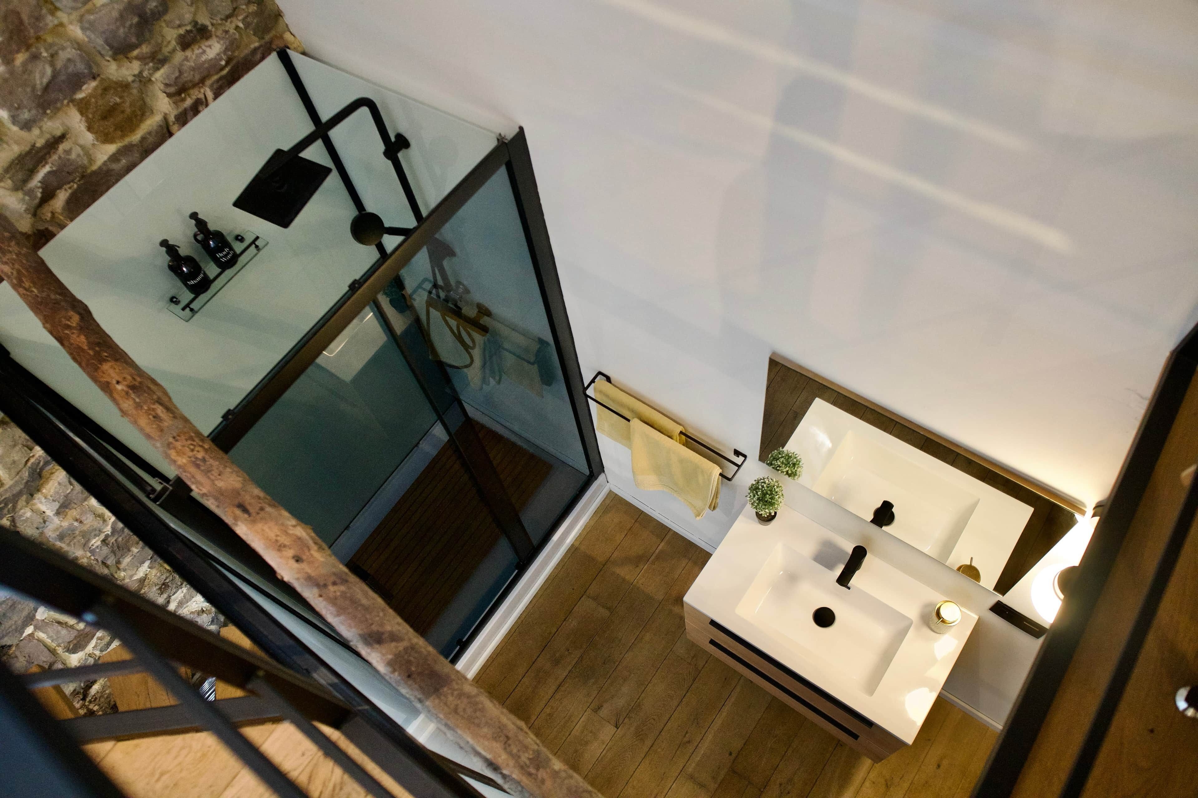 A modern bathroom with a glass shower enclosure, a white sink, and a wooden floor.