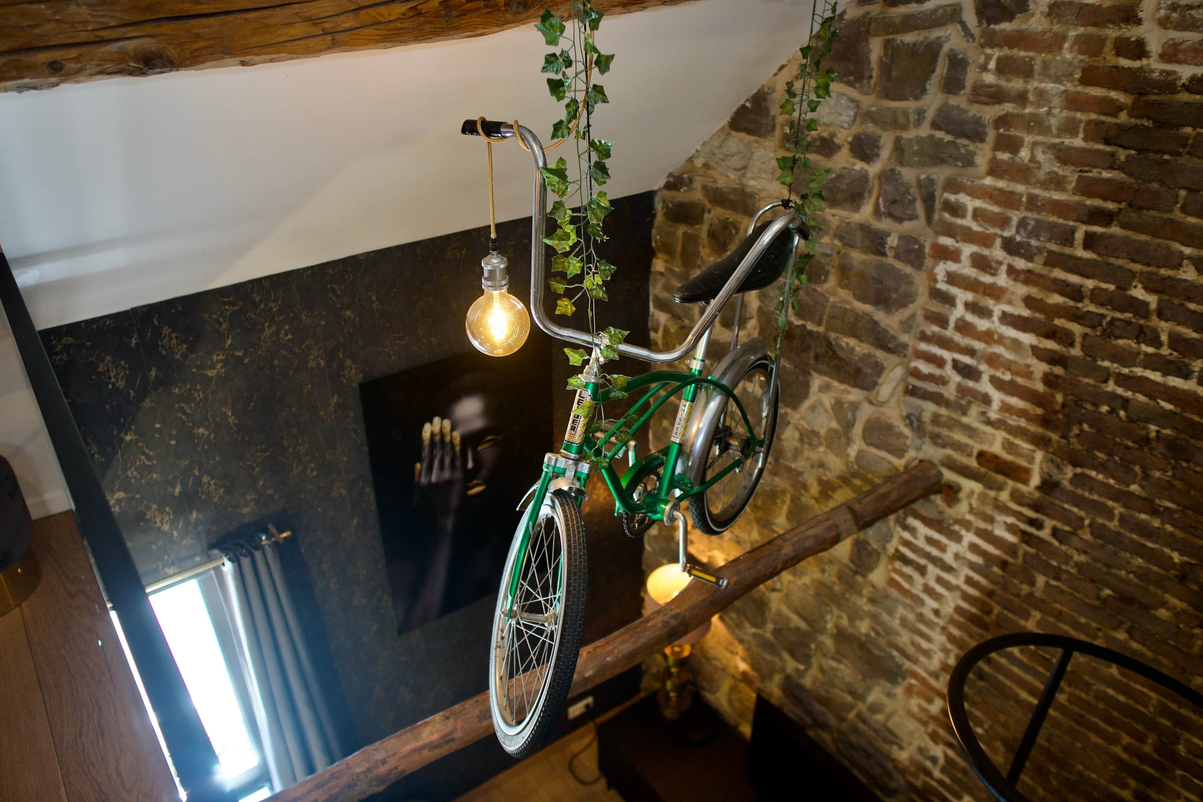 Un vélo suspendu à une poutre en bois, orné de lierre, un mur de pierre et un comptoir noir.