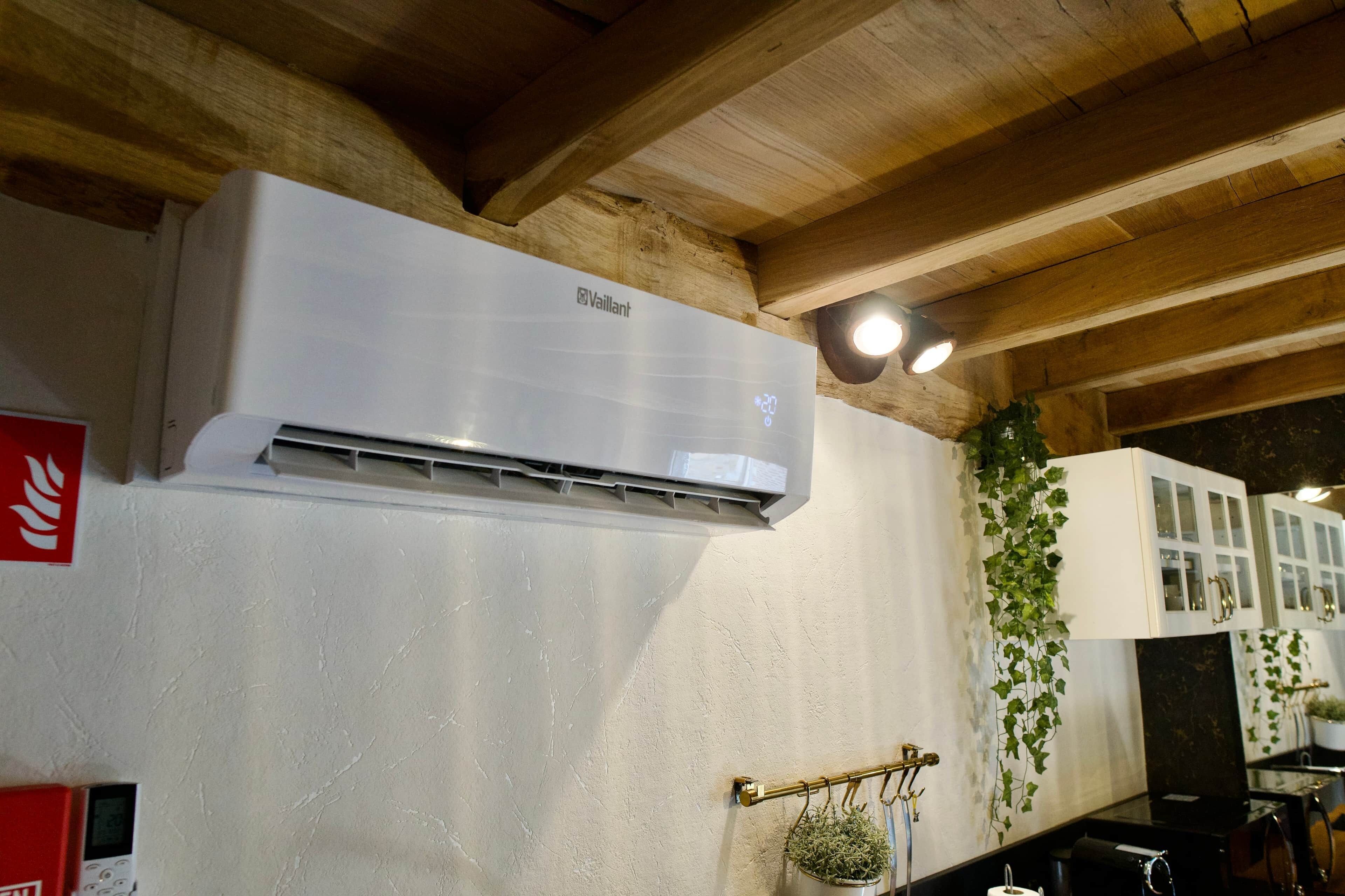 A room with a white air conditioning unit mounted on the wall, a red emergency exit sign, and a potted plant hanging from a brass fixture.