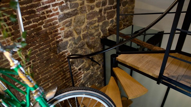 Una escalera con barandilla de madera y pasamanos metálico, que desciende a un nivel inferior.