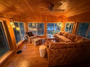 A wooden interior with a ceiling fan, large windows, and a sofa.