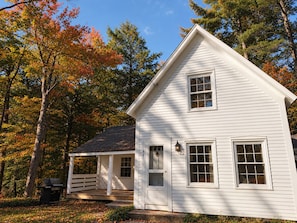 A white two-story house with a porch, a garage, and a yard with trees.