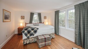 Un dormitorio con cama, lámparas de noche, mesita de noche, ventana con cortinas y cuadros en la pared.
