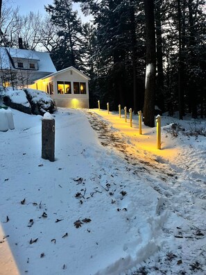 A snow-covered path leading to a building with a porch, surrounded by trees. - Dam Good Times - 90s Lake Getaway (Stoddard)