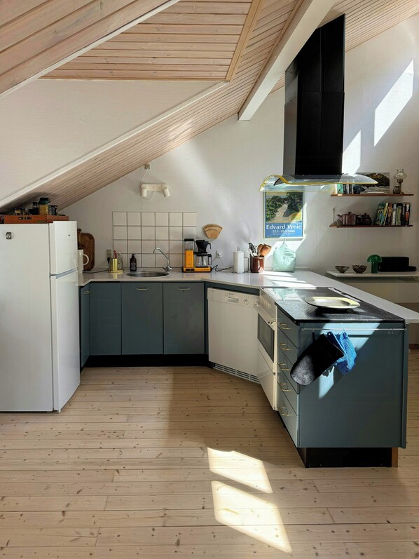 Moderni keittiö, jossa on kalteva katto, integroidut kodinkoneet ja puulattia.