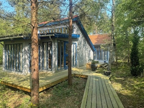 Eine Hütte mit einer Terrasse, einem großen Fenster und einer Tür.