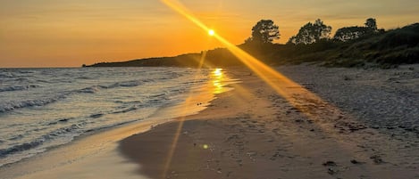 A beach with footprints and the sun setting over the water.