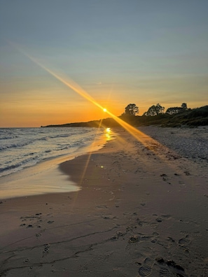 Ein Strand mit Fußspuren und der untergehenden Sonne über dem Wasser.