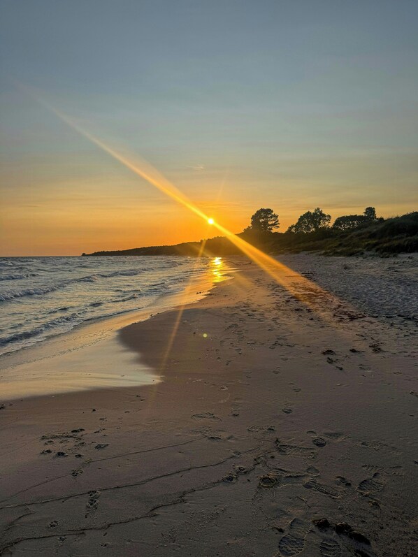 Une plage parsemée d’empreintes et le soleil se couchant sur l’eau.