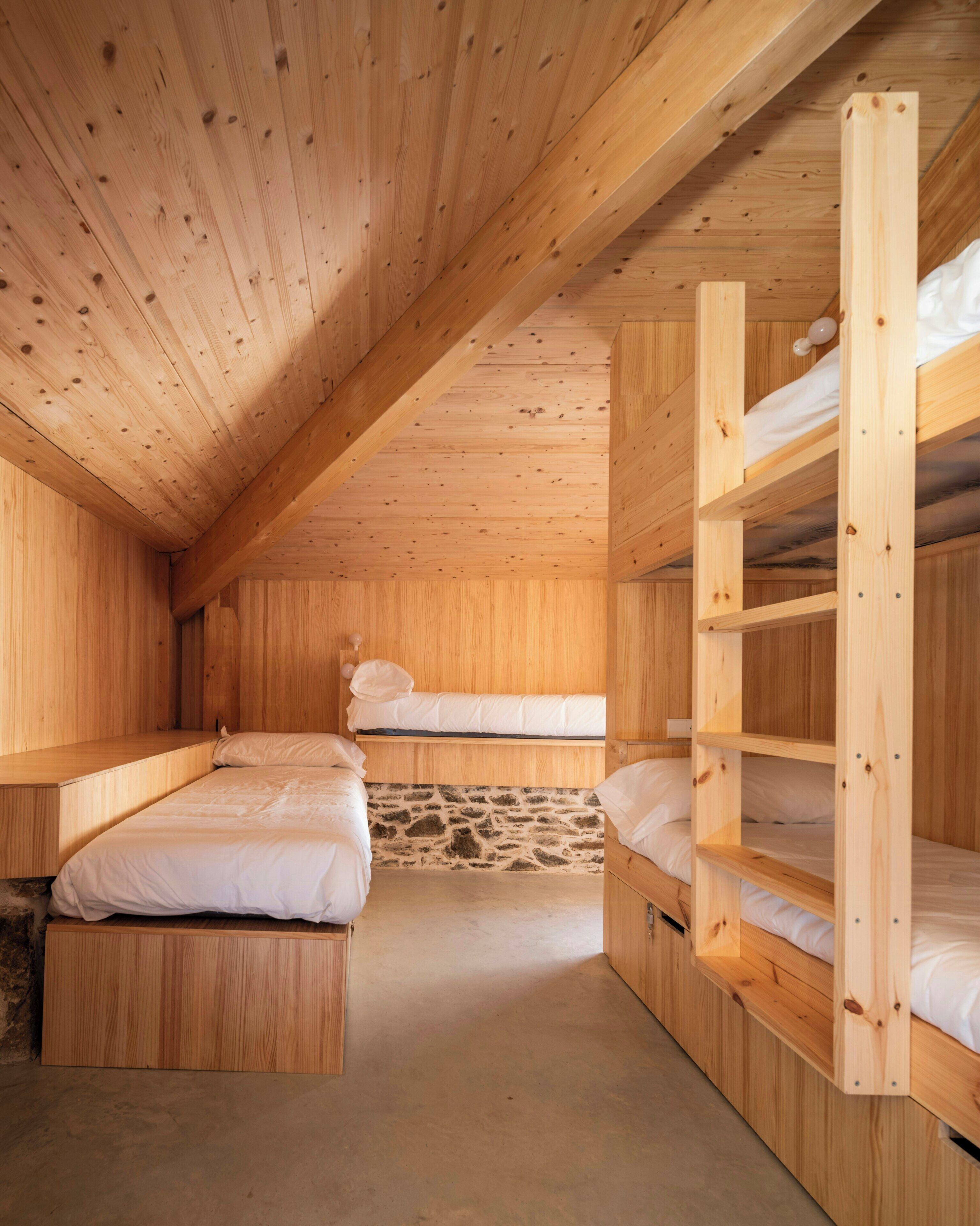 Une cabane en bois avec des lits superposés, un mur en pierre et un plafond en pente.