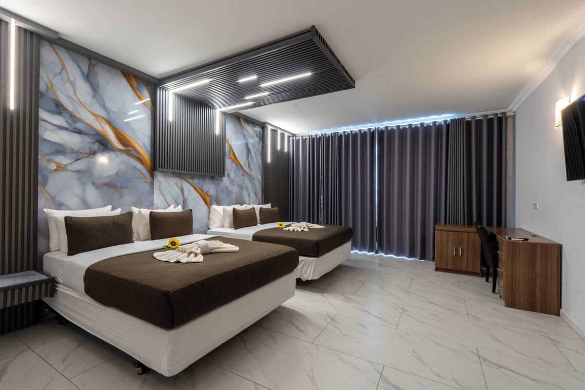 Una habitación de hotel moderna con dos camas, un escritorio y un ventanal grande con cortinas.