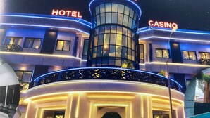 Rakennuksessa on kyltit, joissa lukee »Elegance Hotel» ja »Casino», sen keskellä kohoaa torni ja siellä on myös uima-allasalue.