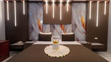A hotel room with a large bed, a heart-shaped towel, a vase with a flower, and a marble-patterned wall.