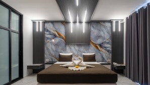 Moderni hotellihuone, jossa on suuri sänky, marmoriseinä ja tyylikäs kattorakenne.