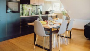 A modern kitchen with a dining area, wooden cabinets, and a built-in oven. - Design apartment with mountain views at Wurmberg (Braunlage)
