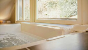 A room with a bathtub, a window with a view of trees, and a towel on the edge of the tub. - Design apartment with mountain views at Wurmberg (Braunlage)