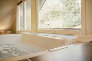 Ein Zimmer mit einer Badewanne, einem Fenster mit Blick auf Bäume und einem Handtuch am Badewannenrand.