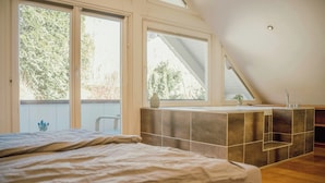 A bedroom with a large bed, a skylight, and a view of trees outside. - Design apartment with mountain views at Wurmberg (Braunlage)