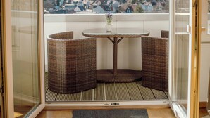 A balcony with wicker furniture, a small table, and a view of a town. - Design apartment with mountain views at Wurmberg (Braunlage)