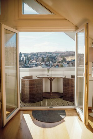 Ein Balkon mit Korbmöbeln, einem kleinen Tisch und Blick auf eine Stadt.