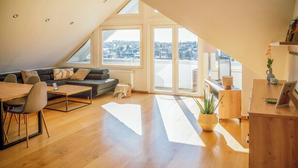 A modern loft with a sloped ceiling, a dining area, a sofa, a coffee table, a potted plant, and a view of the city. - Design apartment with mountain views at Wurmberg (Braunlage)