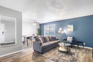 Een moderne woonkamer met een grijze bank, een bijzettafeltje en een blauwe wand.