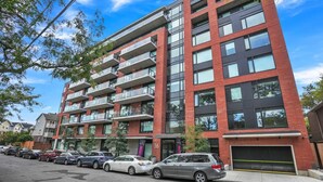 Un edificio residencial de varios pisos con balcones, coches aparcados y un cielo despejado.