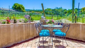 An outdoor patio with a table and chairs, surrounded by a garden with various plants and flowers.