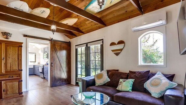 A living room with a glass coffee table, a brown leather sofa, wooden cabinets, and a large window.