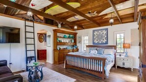 A bedroom with a wooden bed, a TV, a wooden cabinet with dishes, and a ladder.