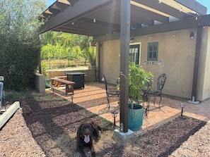 Um alpendre coberto com pérgola, mobiliário de exterior e um cão.