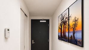 Un corridoio con una porta nera, un termostato e un quadro raffigurante un tramonto.