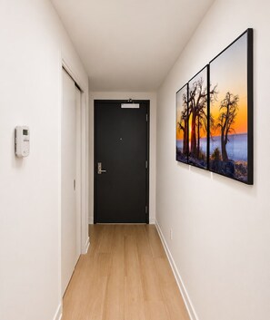 Ein Flur mit einer schwarzen Tür, einem Thermostat und einem Sonnenuntergangsbild an der Wand.