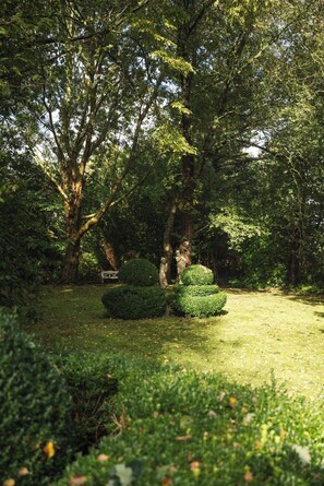 A garden with a bench, trimmed bushes, and a statue.