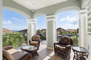Ein Balkon mit Korbmöbeln, einem Glastisch und Blick auf Häuser und Grünflächen.