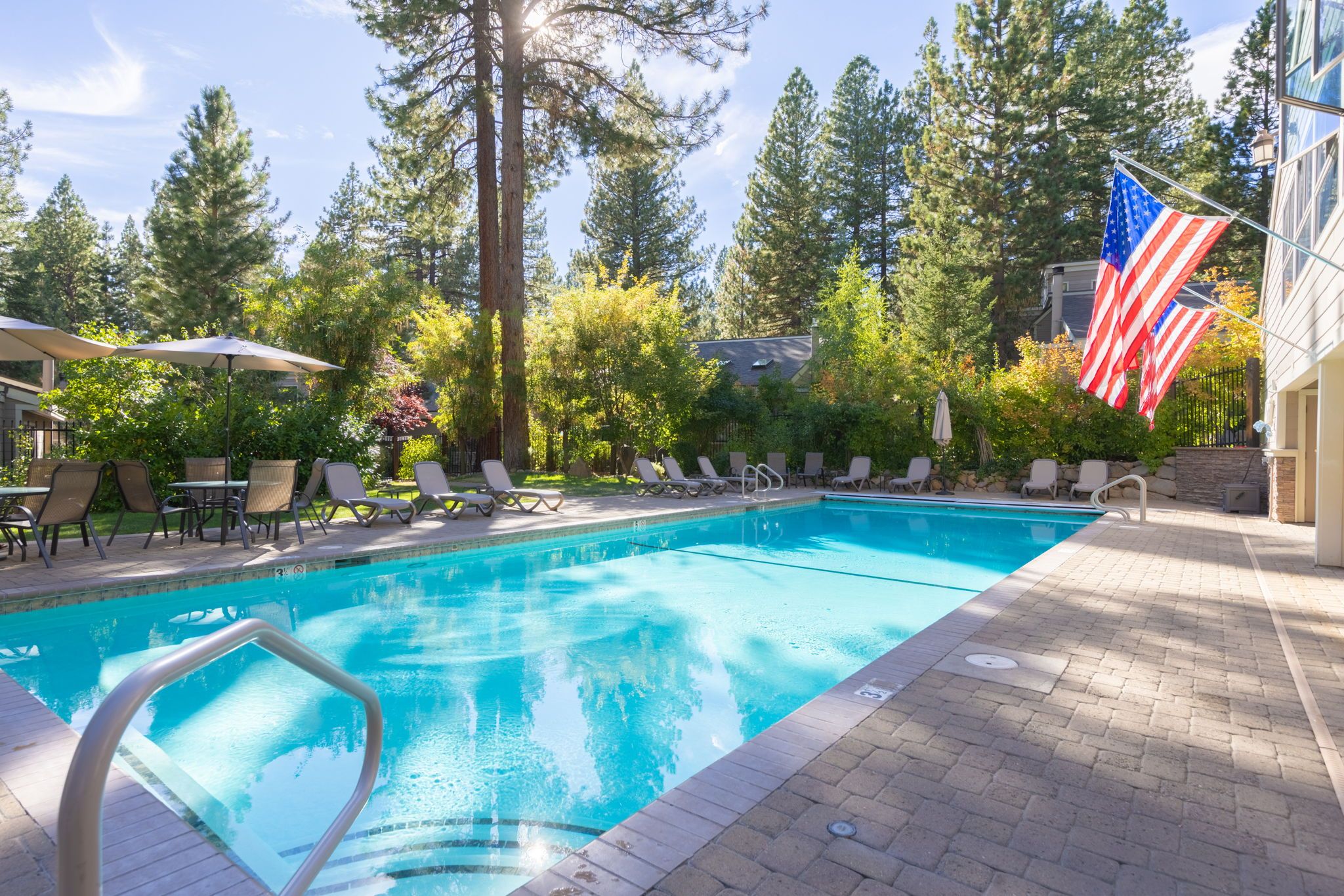 Ein Swimmingpool mit Liegestühlen und Sonnenschirmen, umgeben von Bäumen und einer amerikanischen Flagge.