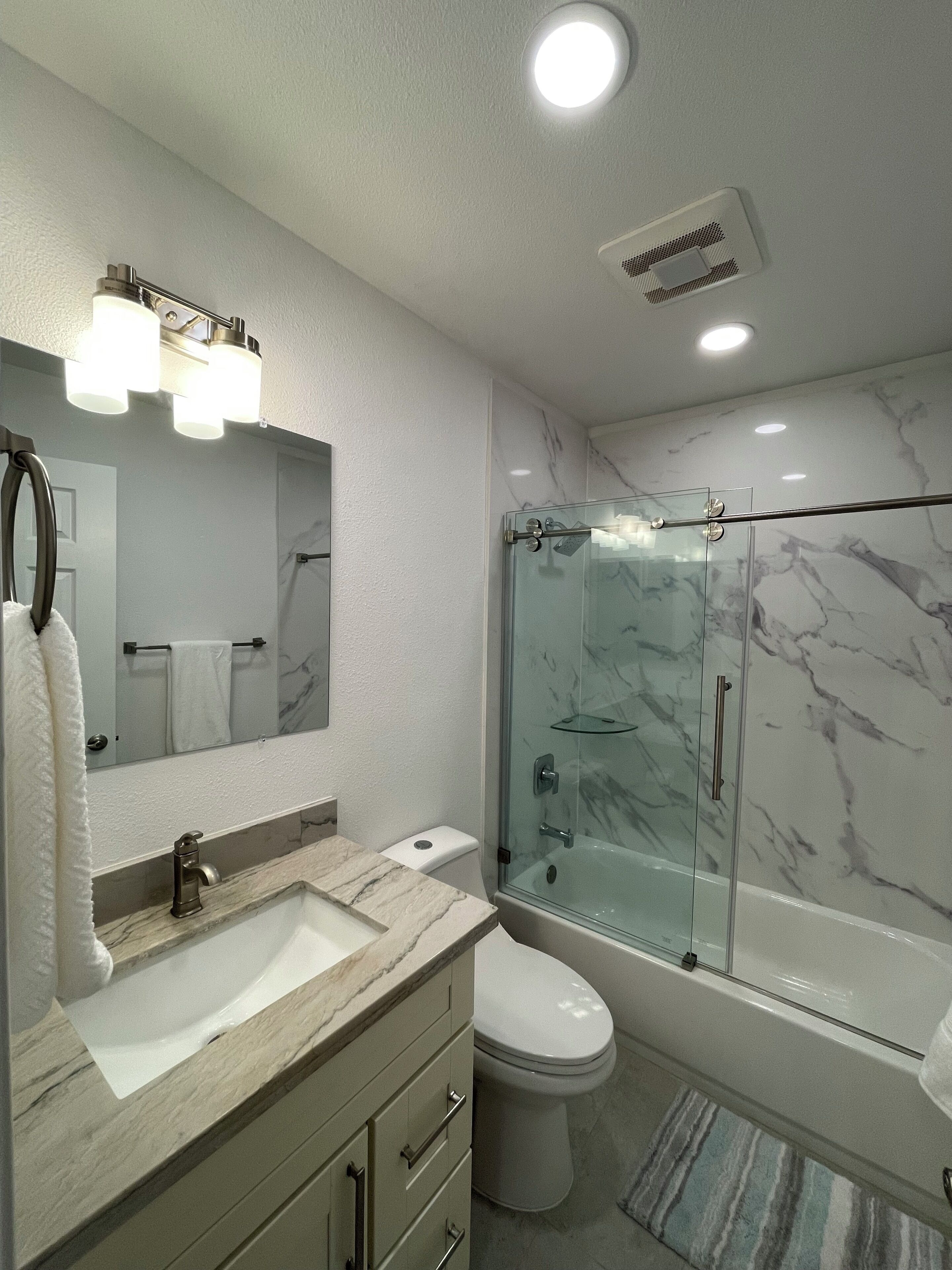 A bathroom with a marble sink, a glass-enclosed shower, a toilet, and a mirror with lights.