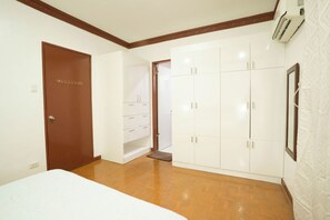 A bedroom with a bed, a wardrobe, a door, and a wall-mounted air conditioner.